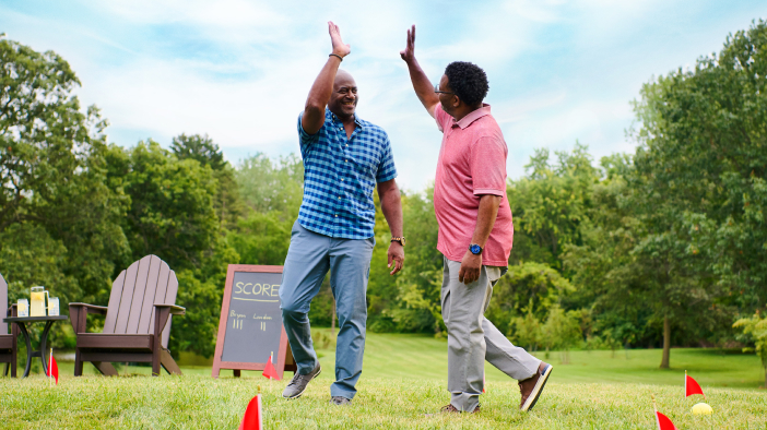 Two smiling men high-five outdoors during a game of bocce ball.