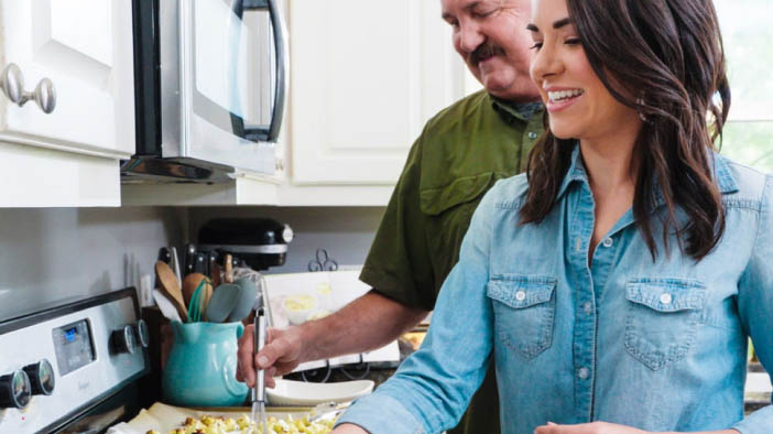Father and daughter cooking together at the stovetop, preparing a meal with visible utensils and ingredients. 