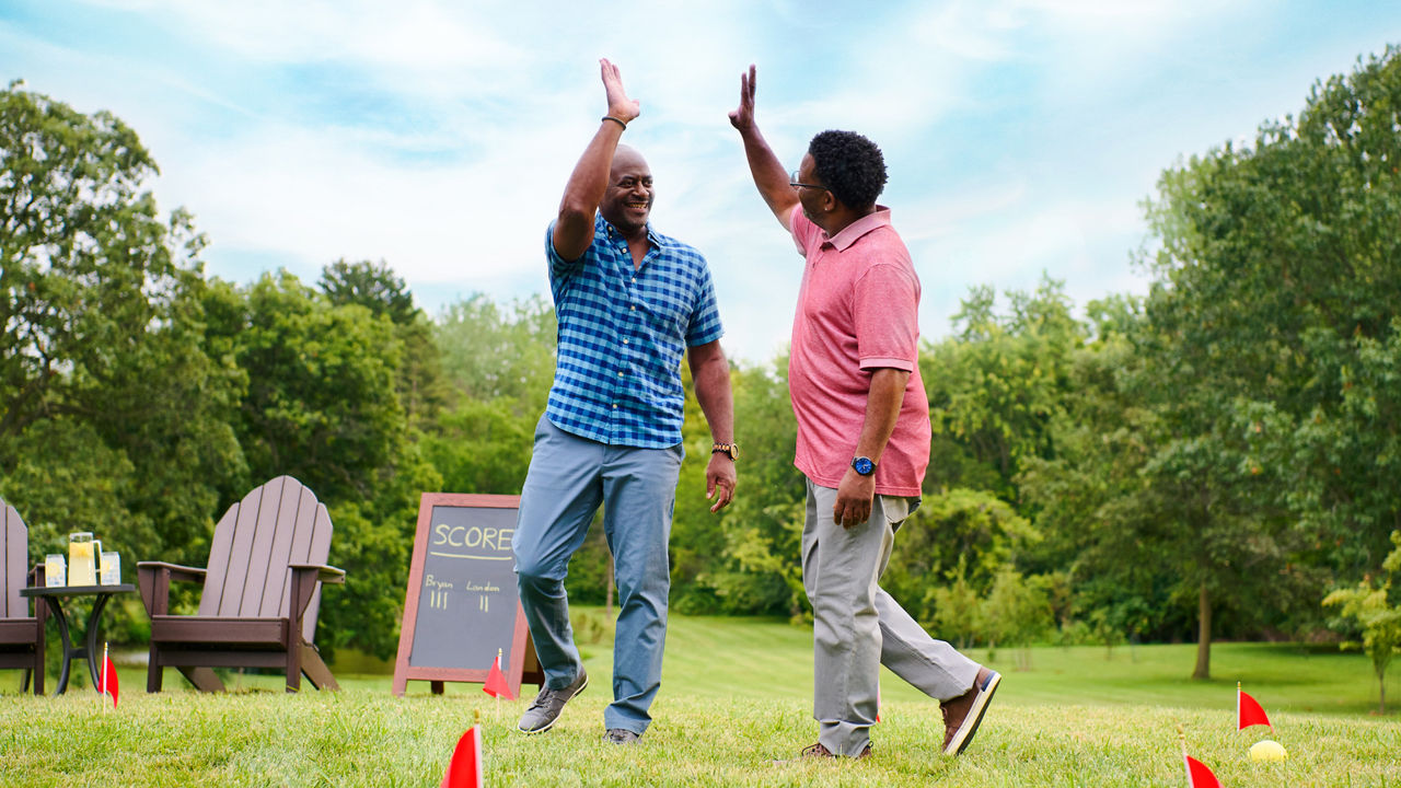 Two smiling men high-five outdoors during a game of bocce ball.